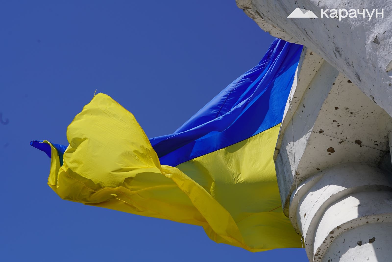 Український прапор на тлі посіченого осколками пам’ятника Артему